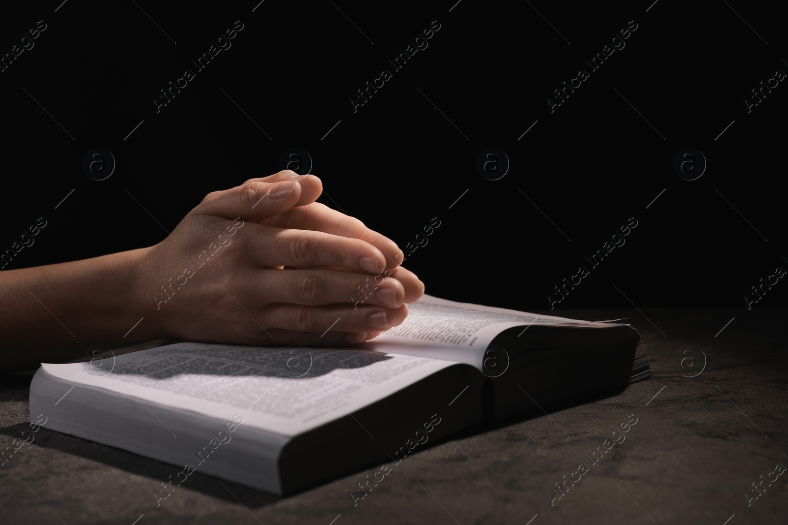 Photo of Religion. Christian woman praying over Bible at table against black background, closeup. Space for text