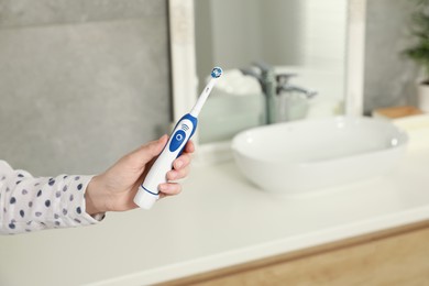 Woman holding electric toothbrush in bathroom at home, closeup. Space for text