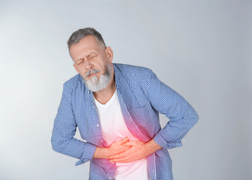 Image of Mature man suffering from abdominal pain on light background