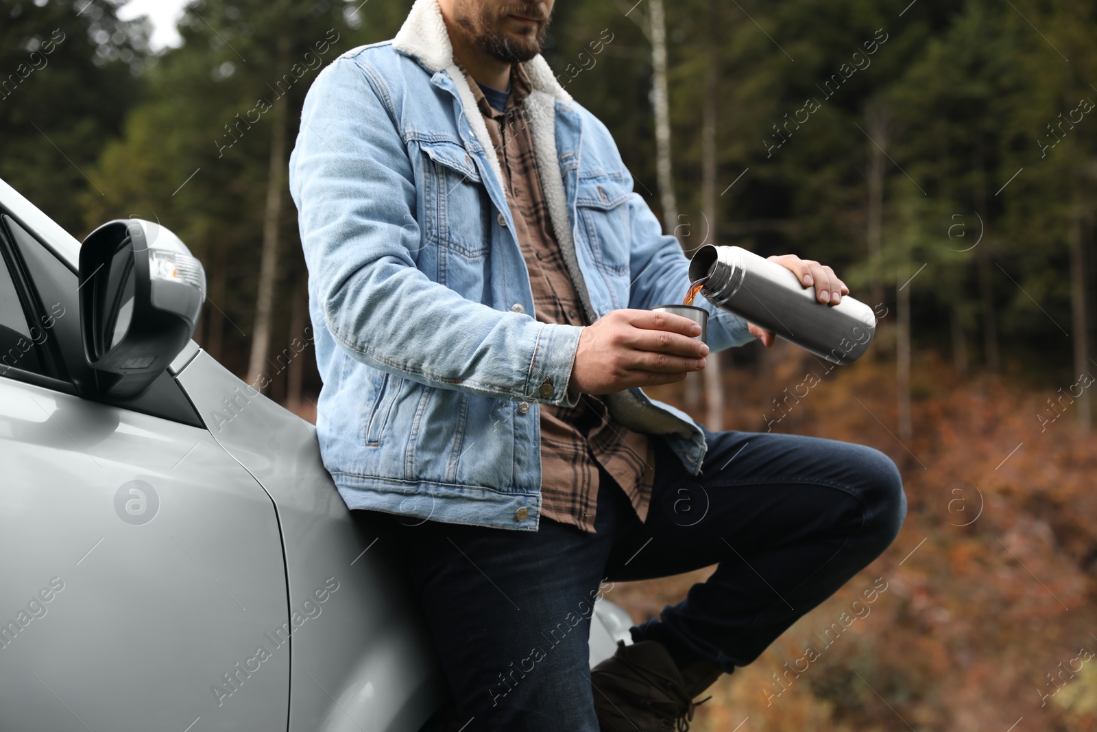 Photo of Man pouring hot drink from metallic thermos into cup lid near car, closeup