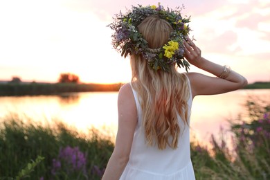 Photo of Young woman wearing wreath made of flowers outdoors at sunset