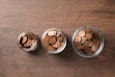 Photo of Glass jars with coins on wooden table, flat lay