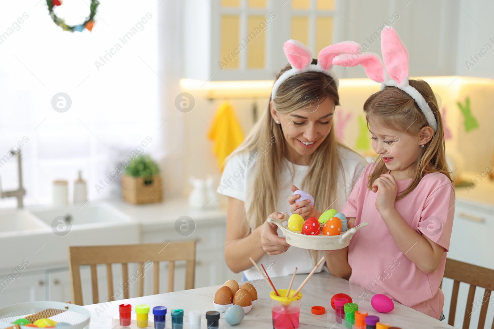 Photo of Easter celebration. Happy mother and her cute daughter with painted eggs at white marble table in kitchen