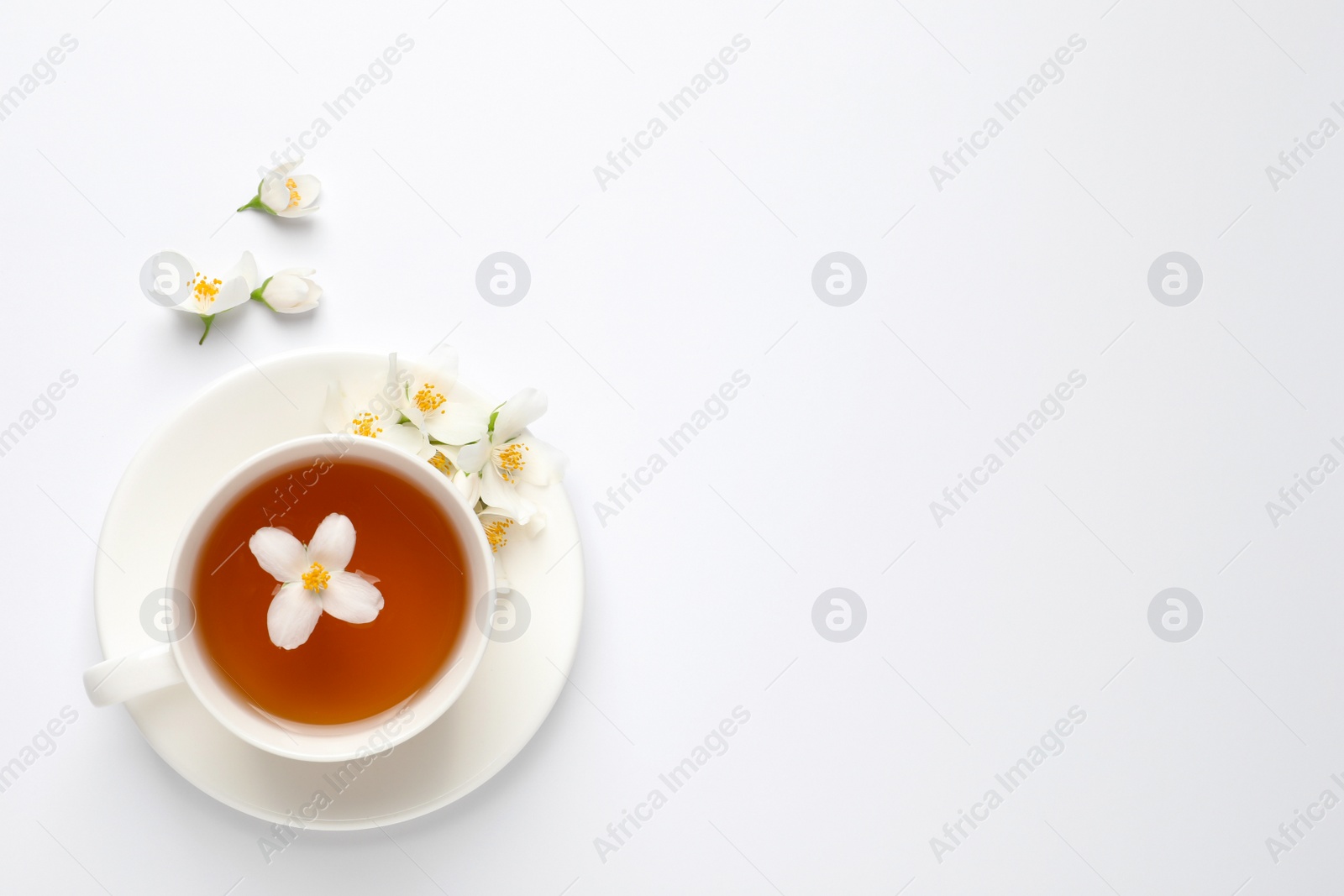 Photo of Cup of aromatic jasmine tea and fresh flowers on white background, top view. Space for text