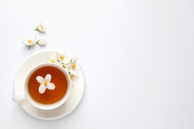 Cup of aromatic jasmine tea and fresh flowers on white background, top view. Space for text