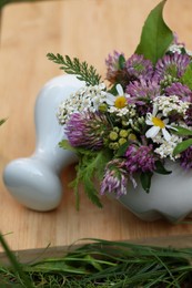 Photo of Ceramic mortar with pestle, different wildflowers and herbs on green grass, closeup