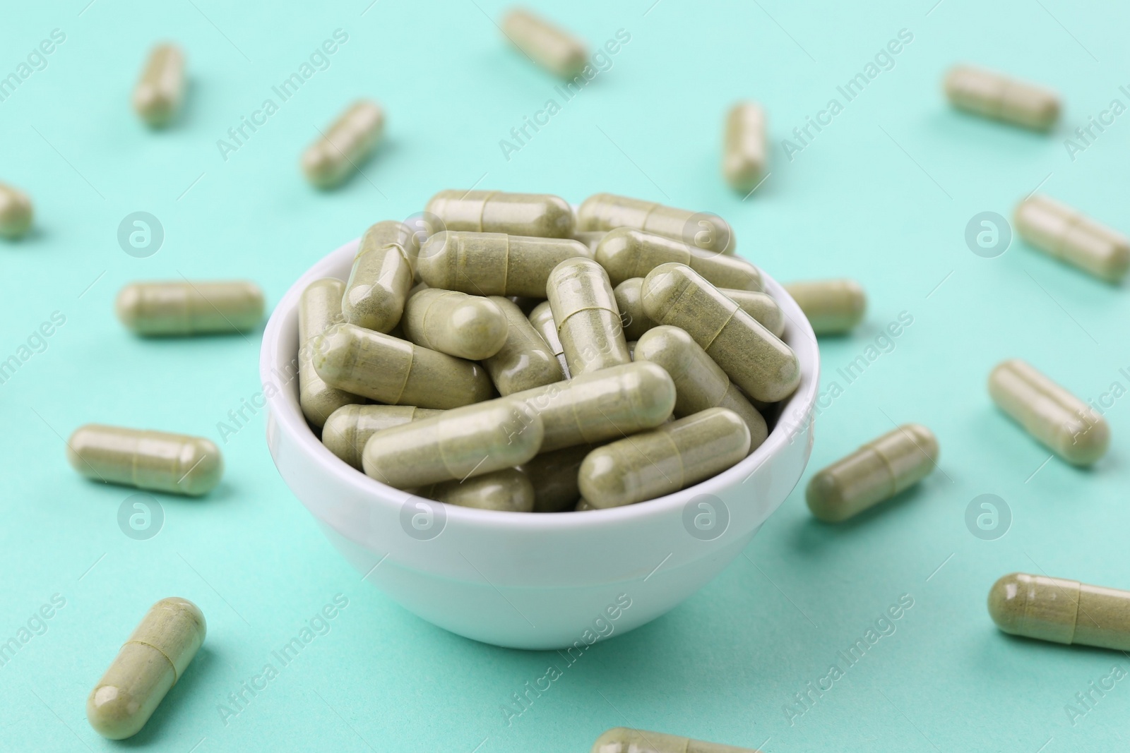 Photo of Bowl with vitamin capsules on turquoise background, closeup