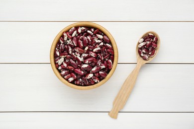 Photo of Bowl and spoon with dry kidney beans on white wooden table, flat lay