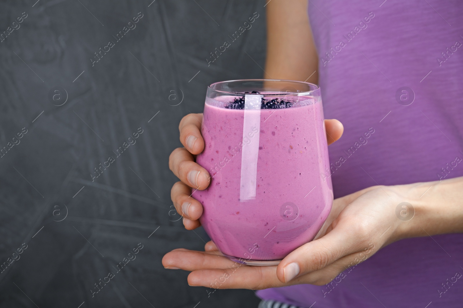 Photo of Young woman holding glass of tasty blackberry smoothie on grey background, closeup