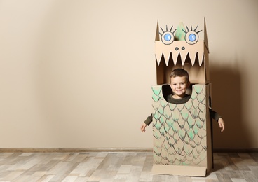 Photo of Cute little boy in cardboard costume of dinosaur near color wall. Space for text