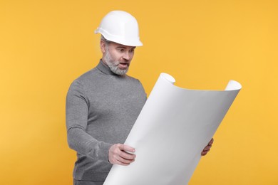 Photo of Emotional architect in hard hat holding draft on orange background