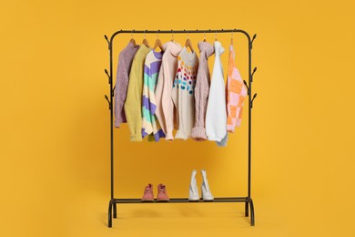 Photo of Rack with stylish women's sweaters on wooden hangers and shoes against orange background