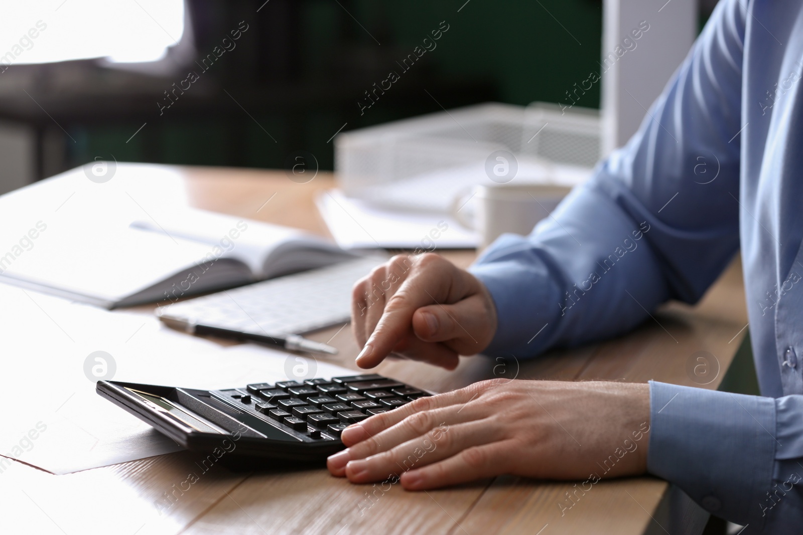 Photo of Man using calculator at wooden table indoors, closeup