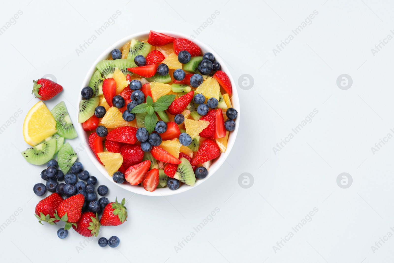 Photo of Yummy fruit salad in bowl and ingredients on light blue background, flat lay. Space for text