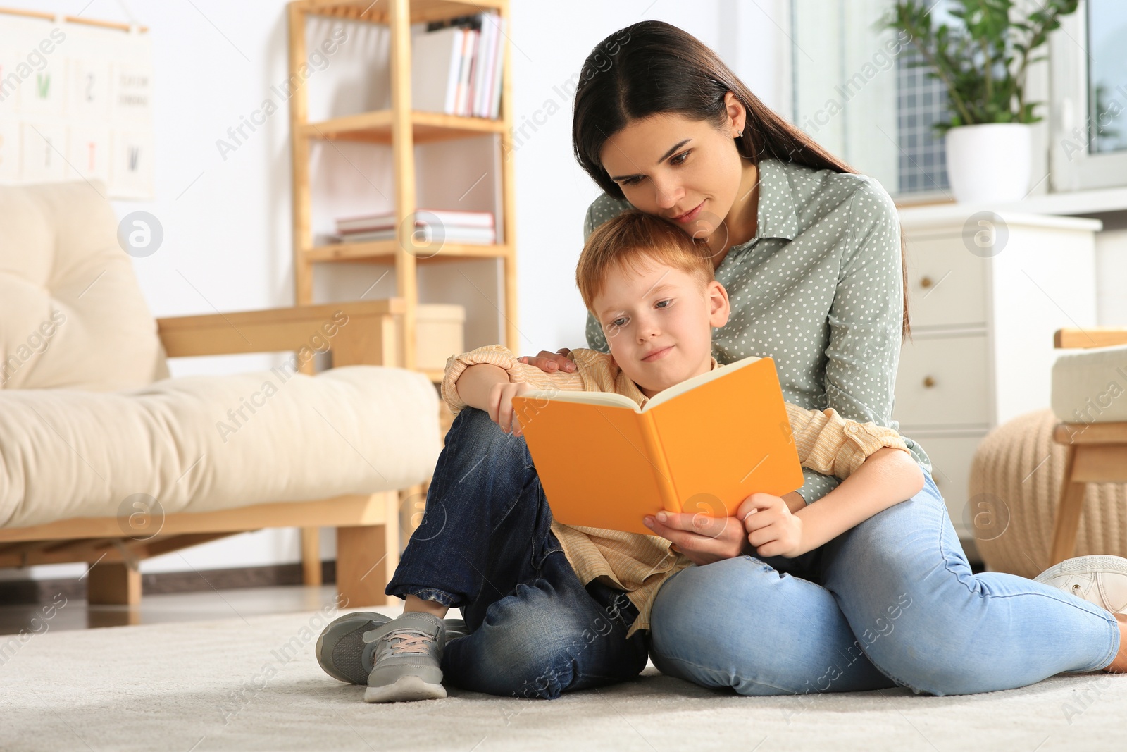 Photo of Mother reading book with her son on floor in living room at home