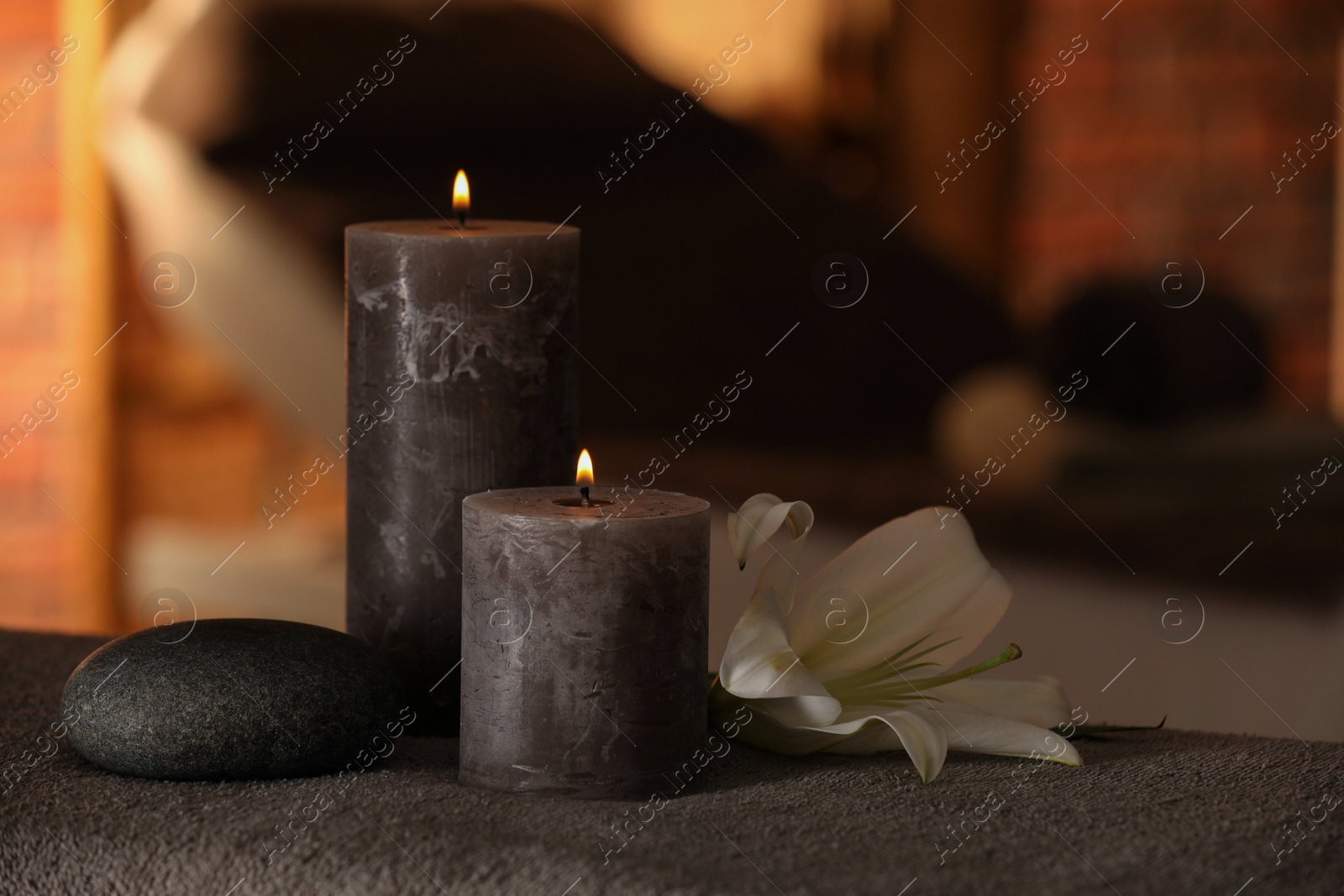 Photo of Spa composition with burning candles, lily flower and stone on massage table in wellness center, space for text