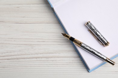 Beautiful fountain pen and notebook on white wooden table, top view. Space for text