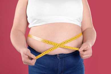 Photo of Overweight woman measuring waist with tape on color background, closeup