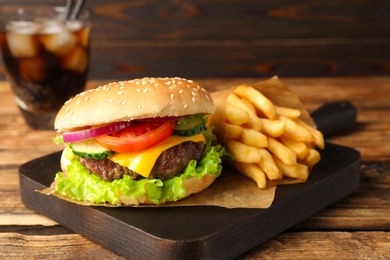 Delicious burger, soda drink and french fries served on wooden table, closeup