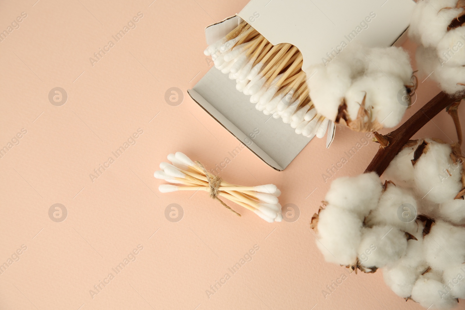 Photo of Cardboard box with cotton buds and flowers on beige background, flat lay. Space for text