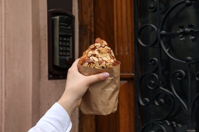 Photo of Woman holding delicious croissant near door, closeup