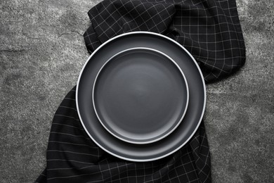 Photo of New dark plates and napkin on grey table, top view