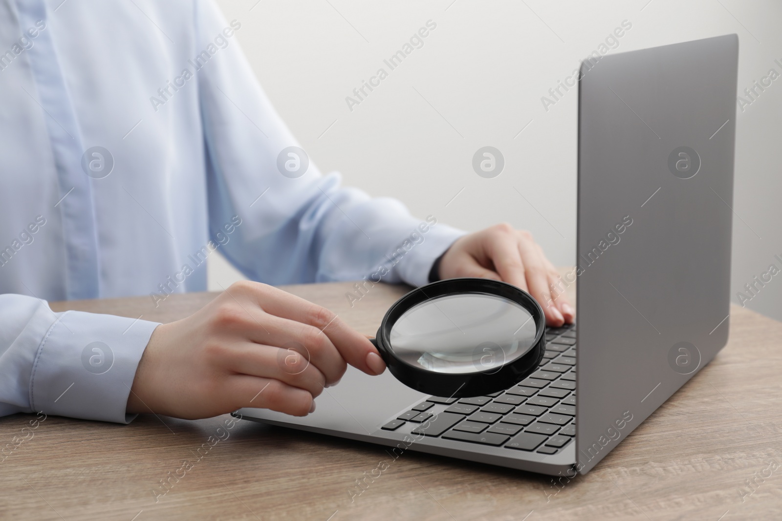 Photo of Woman holding magnifier near laptop at wooden table, closeup. Online searching concept