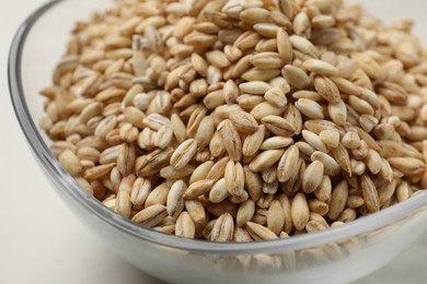 Photo of Dry pearl barley in bowl on white table, closeup