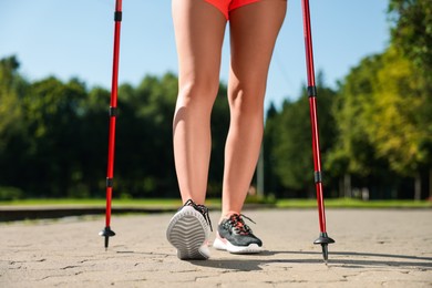 Photo of Woman practicing Nordic walking with poles in park on sunny day, closeup