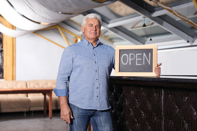 Senior business owner holding OPEN sign in his restaurant