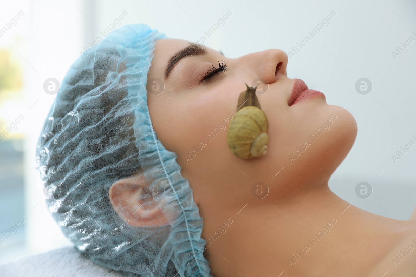 Photo of Young woman receiving snail facial massage in spa salon, closeup