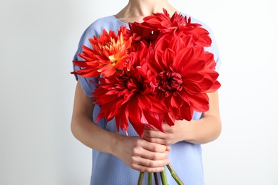 Woman holding bouquet of beautiful dahlia flowers against light background