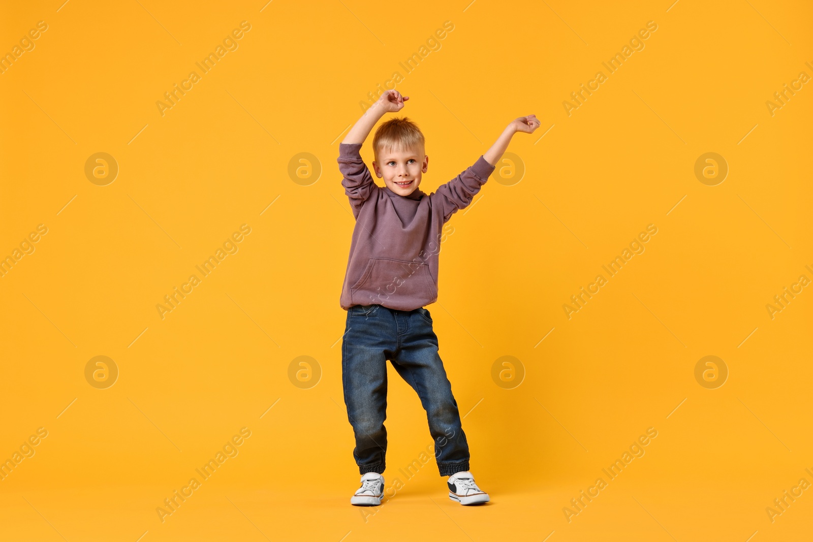 Photo of Happy little boy dancing on yellow background. Space for text