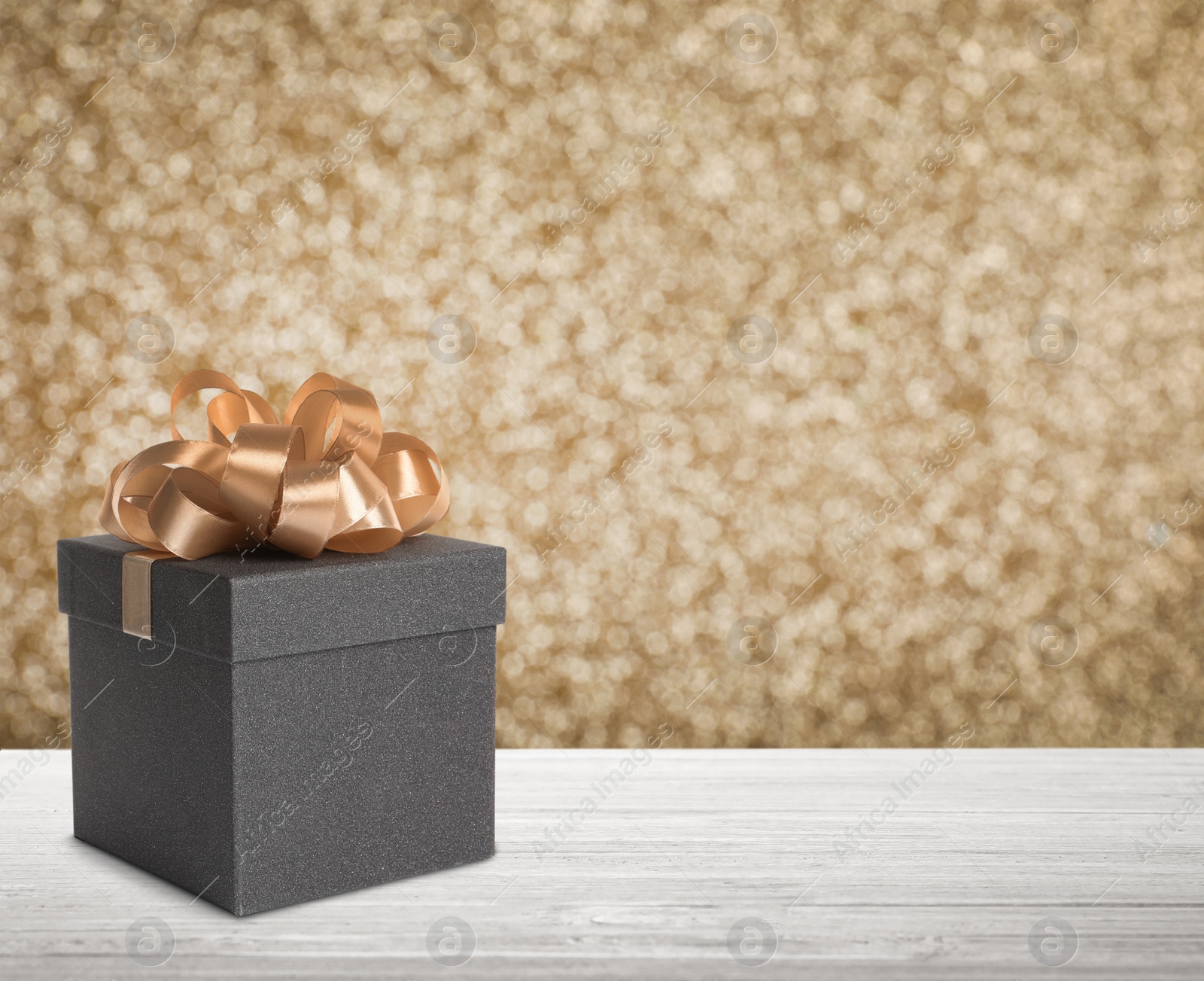 Image of Beautiful gift box on white wooden table against shiny golden background, bokeh effect. Space for text