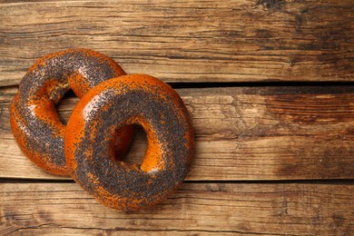 Photo of Delicious fresh bagels with poppy seeds on wooden table, flat lay. Space for text