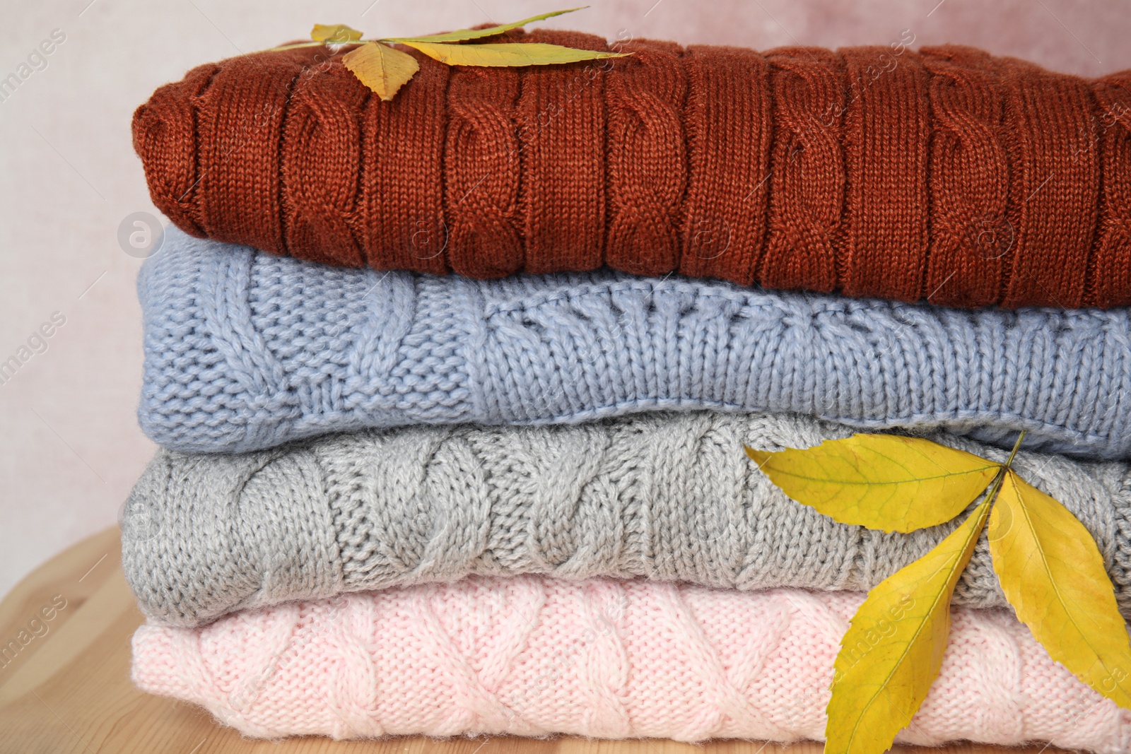 Photo of Stack of warm knitted clothes and autumn leaves on wooden table, closeup