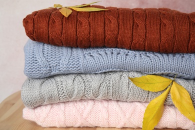 Photo of Stack of warm knitted clothes and autumn leaves on wooden table, closeup