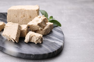 Pieces of tasty halva and mint served on light grey table, closeup. Space for text