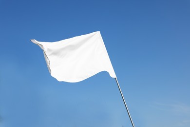 Photo of White flag fluttering against blue sky on sunny day