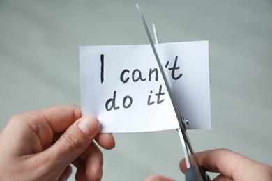 Woman cutting paper with text I can't do it on blurred background, closeup