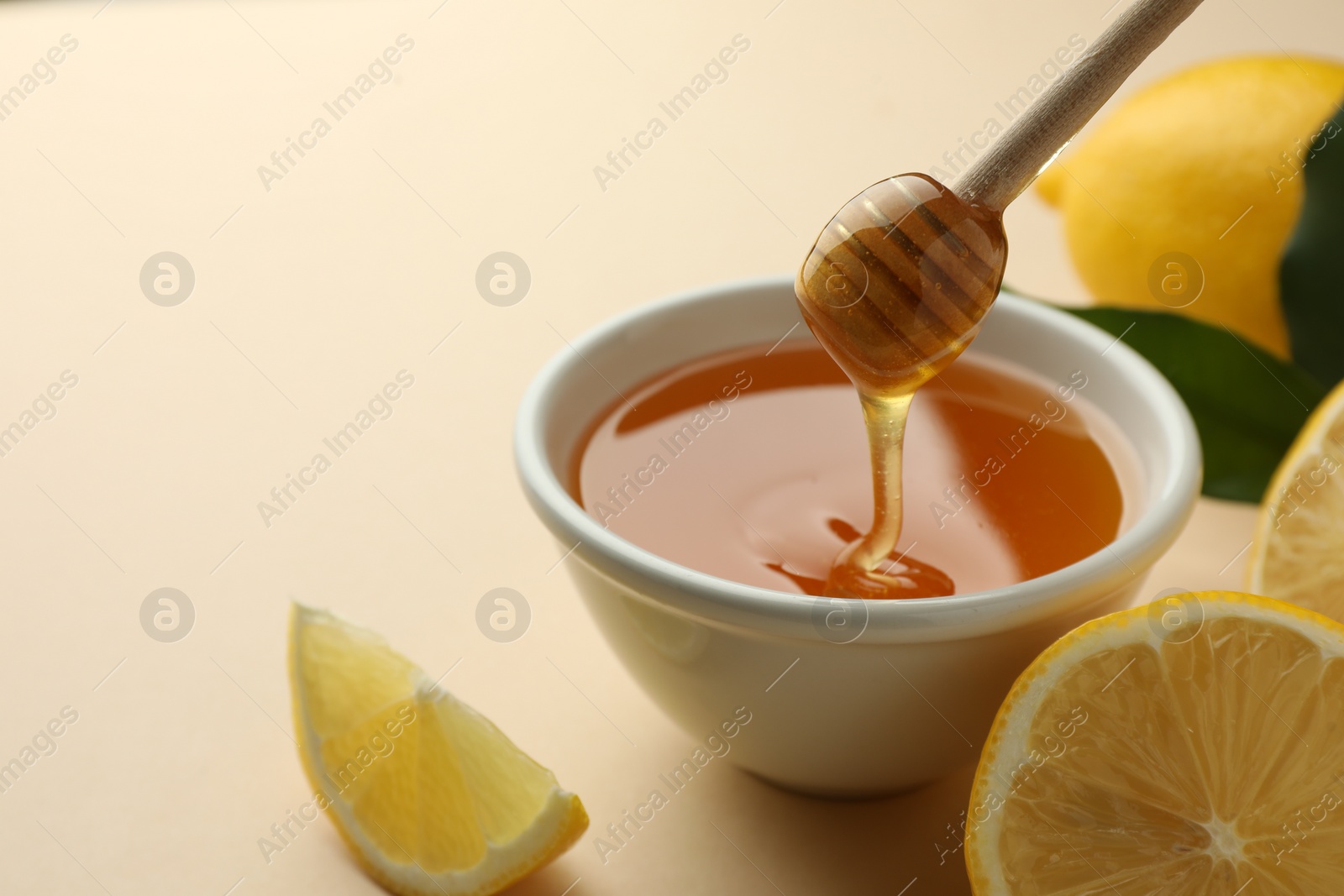 Photo of Pouring tasty honey from dipper into bowl and lemons on beige background, closeup. Space for text