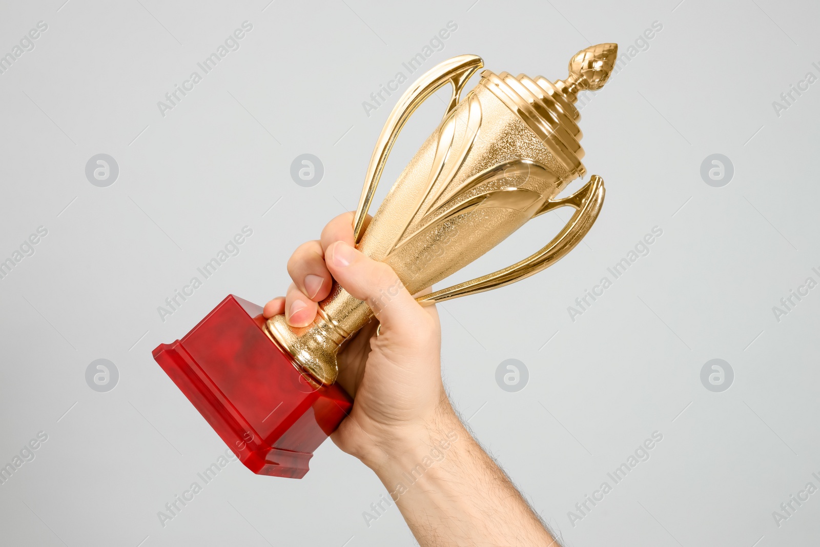 Photo of Man holding gold trophy cup on light grey background, closeup