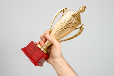 Man holding gold trophy cup on light grey background, closeup