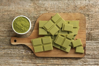 Pieces of tasty matcha chocolate bar and powder in spoon on wooden table, flat lay