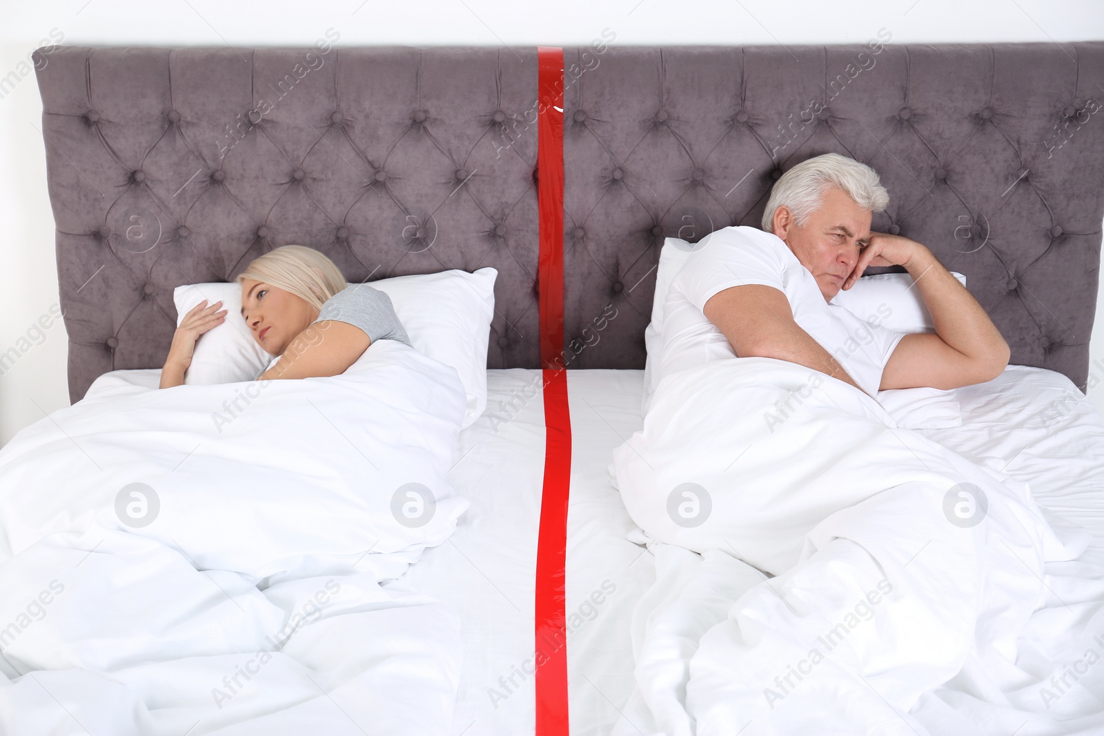 Photo of Upset mature couple with relationship problems lying separately in bed at home