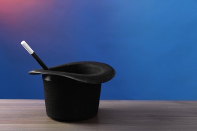 Magician's hat and wand on wooden table against color background, space for text