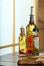Photo of Cooking oil with different spices and herbs in bottles on wooden table