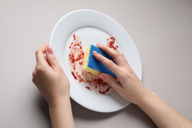 Woman washing dirty plate with sponge on light grey background, closeup