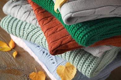 Photo of Stack of knitted clothes and autumn leaves on wooden background, closeup