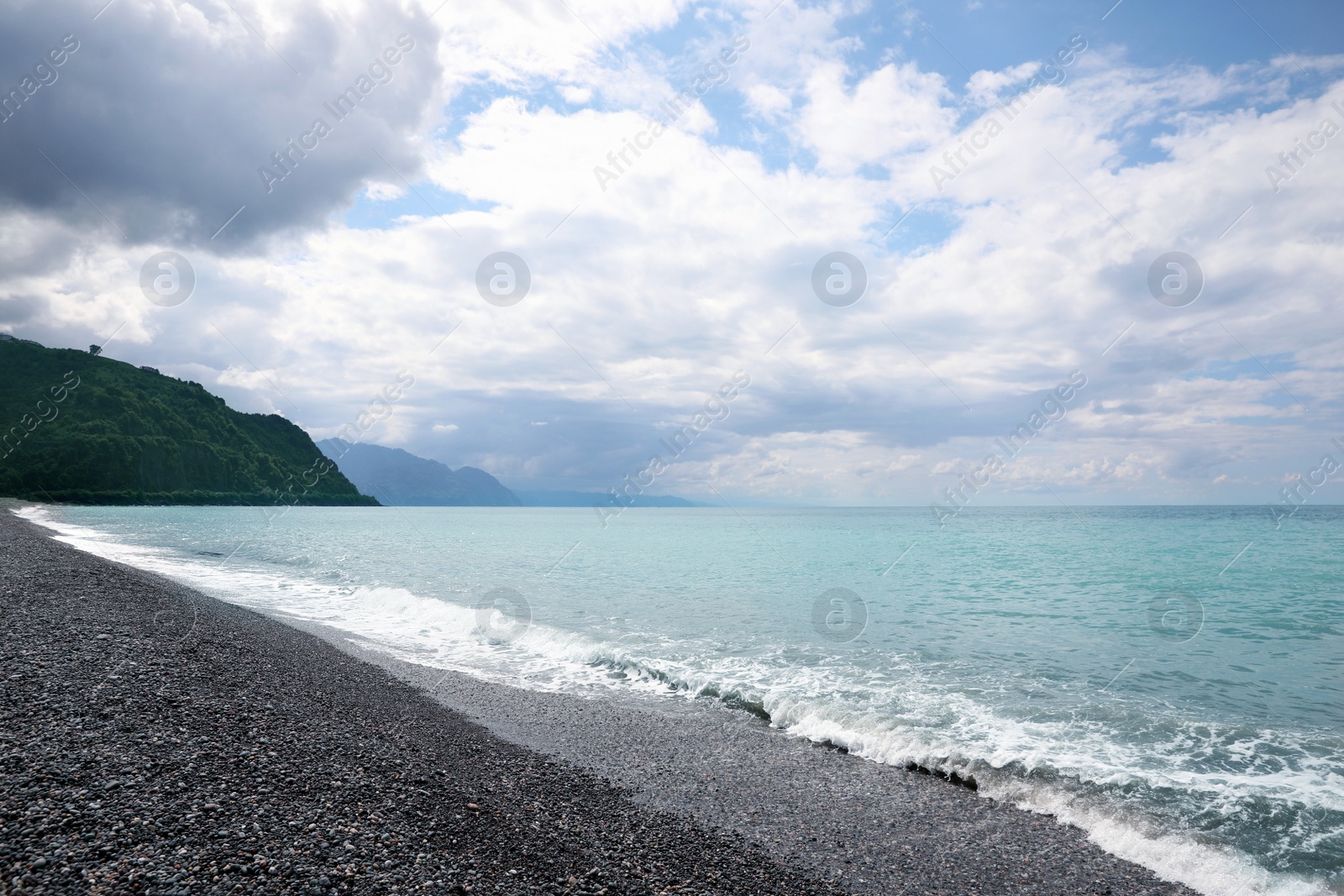 Photo of Picturesque view of beautiful sea shore and mountains under sky with fluffy clouds